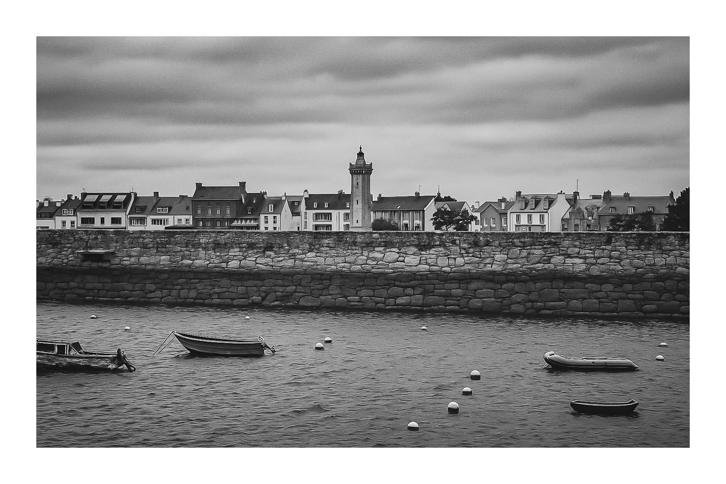 Vue du bassin de Roscoff, jetée en granit, bouées et embarcations avec une tour/clé de clocher en arrière-plan, noir et blanc avec bordure