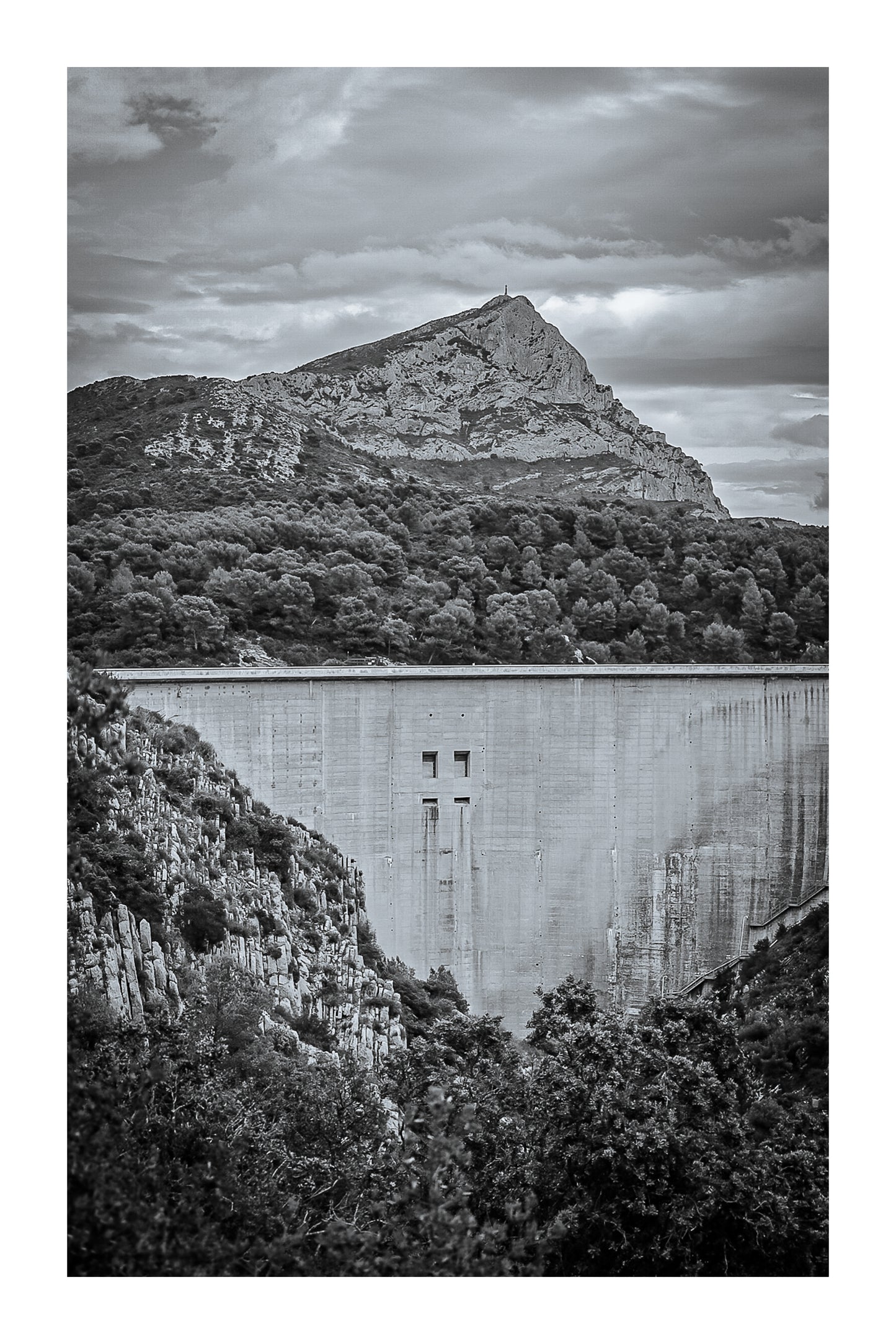Barrage massif au premier plan avec la Sainte-Victoire en arrière-plan, forêt méditerranéenne et ciel nuageux, noir et blanc avec bordure