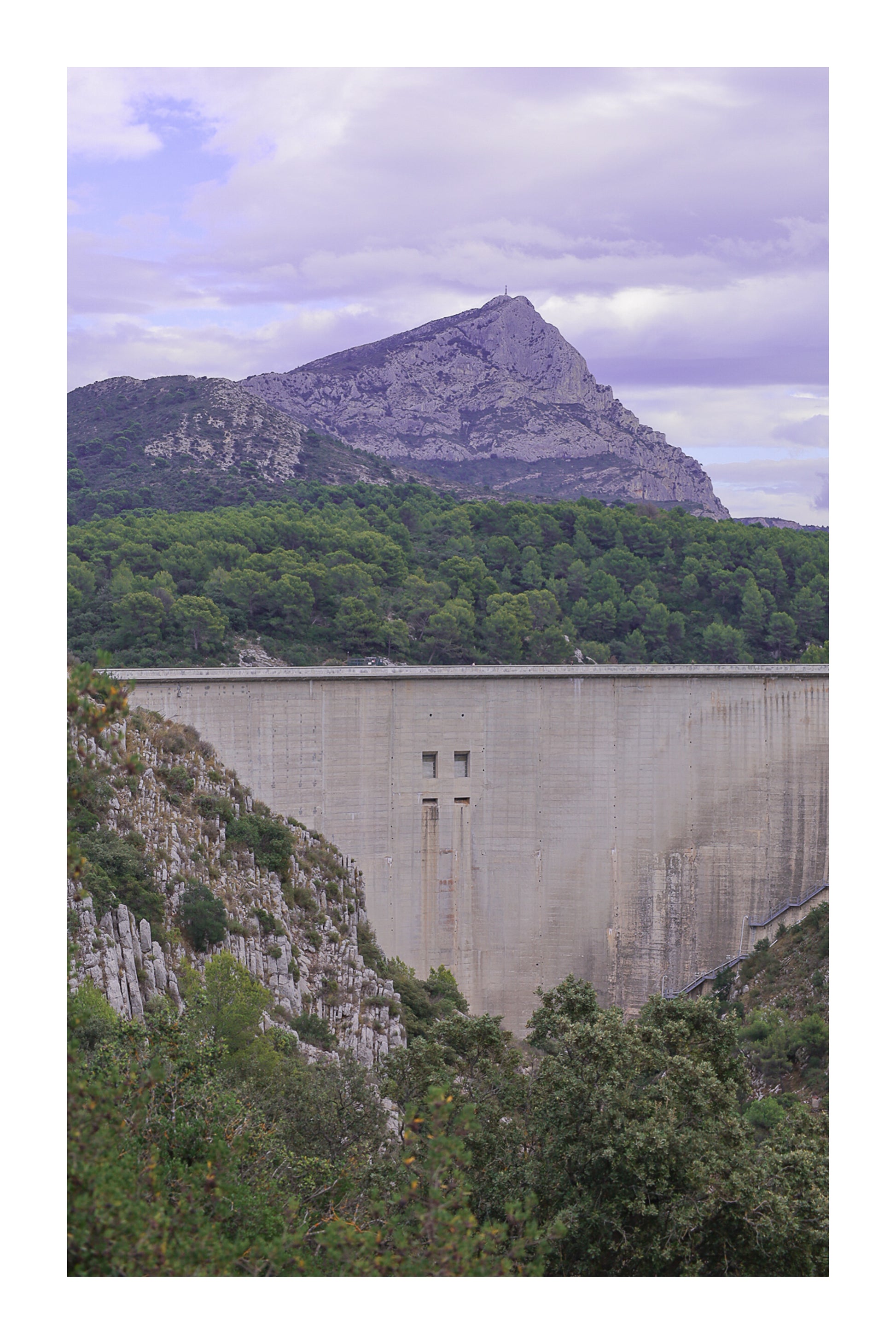 Barrage massif au premier plan avec la Sainte-Victoire en arrière-plan, forêt méditerranéenne et ciel nuageux avec bordure