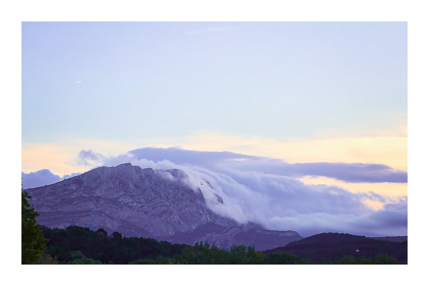 Sainte-Victoire au crépuscule avec nuages en cascade sur les crêtes, avant-plans sombres de collines et d’arbres avec bordure