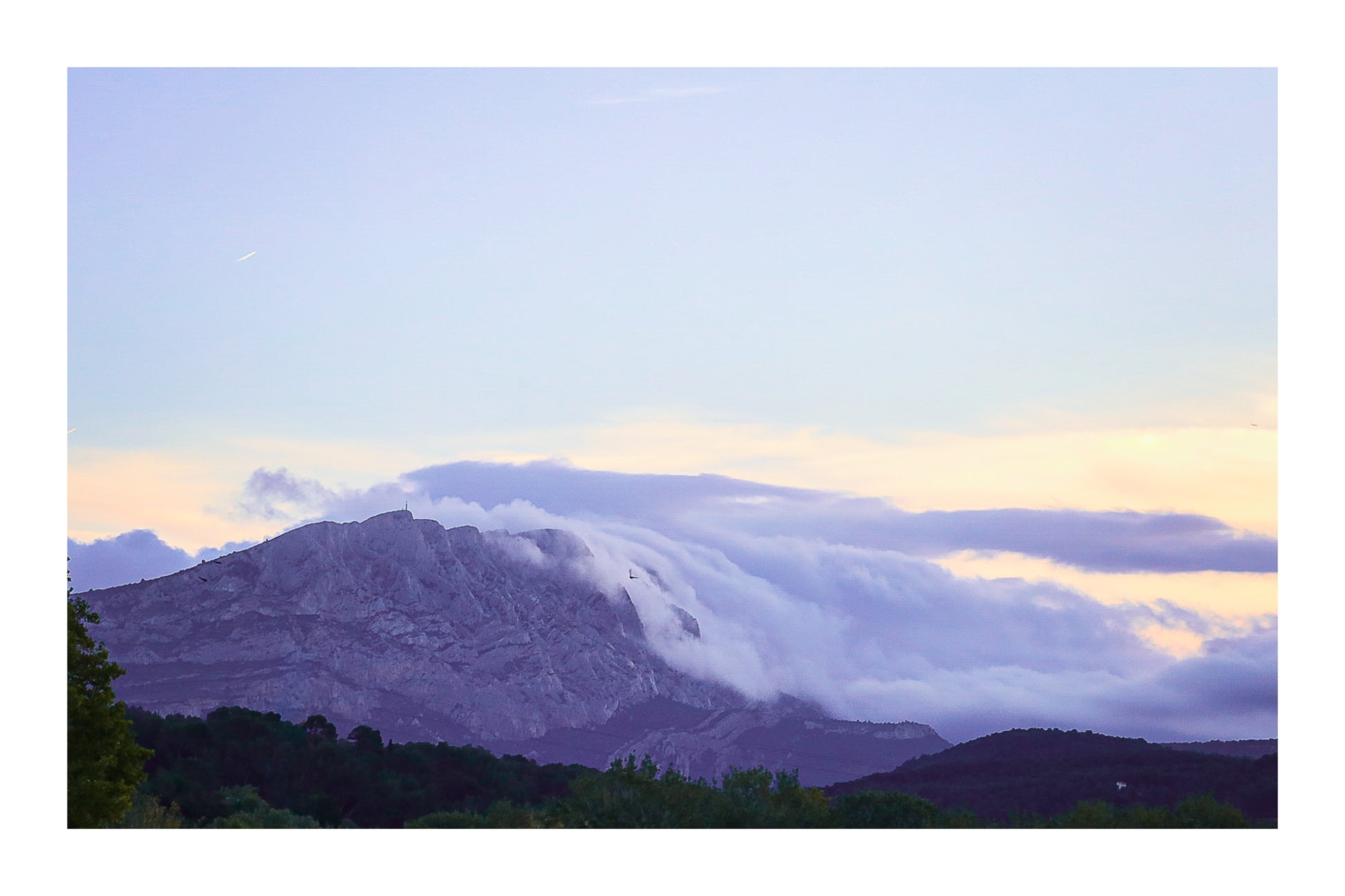 Sainte-Victoire au crépuscule avec nuages en cascade sur les crêtes, avant-plans sombres de collines et d’arbres avec bordure