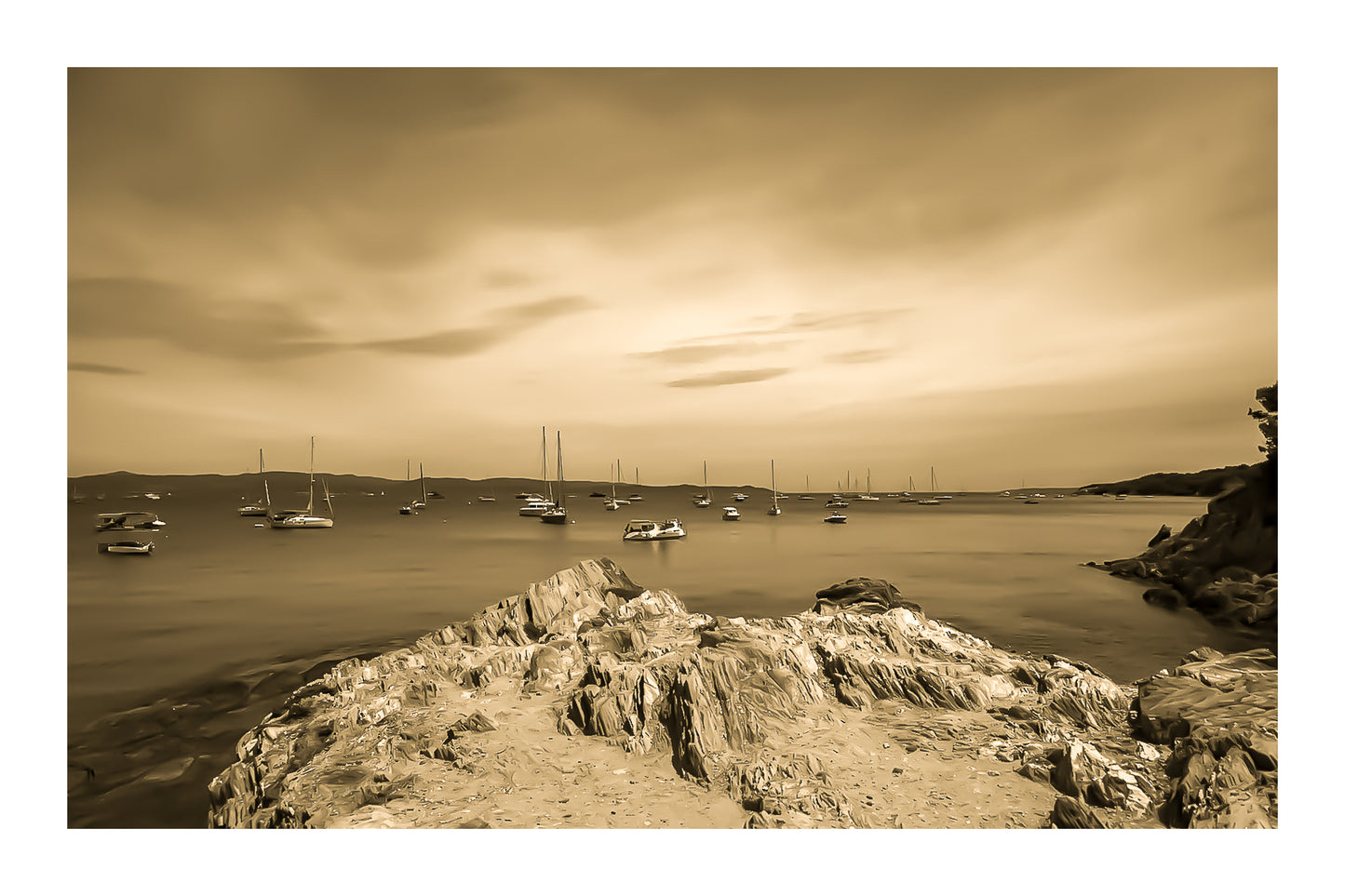 Avant-plan de roches sculptées et ligne de bateaux au large, ciel voilé à la presqu’île de Giens, style vintage sépia avec bordure