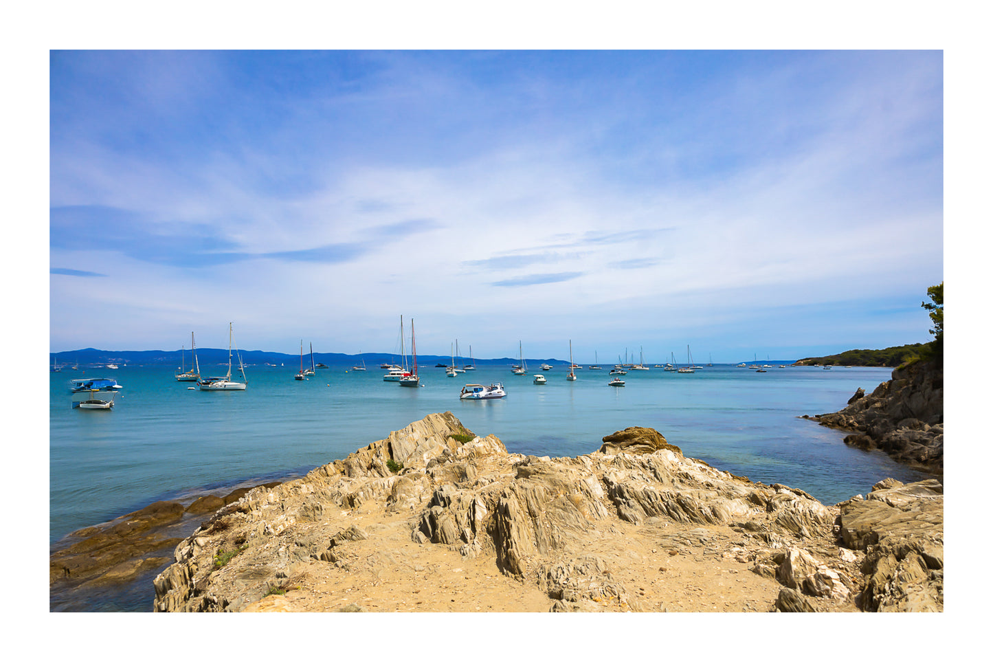 Avant-plan de roches sculptées et ligne de bateaux au large, ciel voilé à la presqu’île de Giens, couleur avec bordure