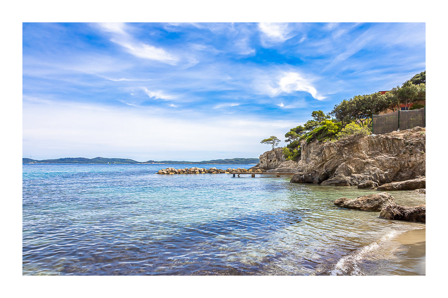 Petite crique bordée de rochers et pins, mer calme et nuages texturés à Giens, couleur avec bordure