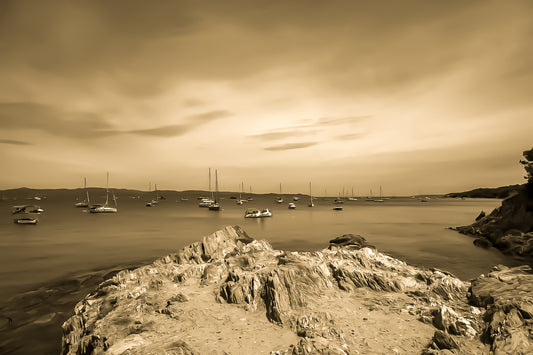 Avant-plan de roches sculptées et ligne de bateaux au large, ciel voilé à la presqu’île de Giens, style vintage sépia