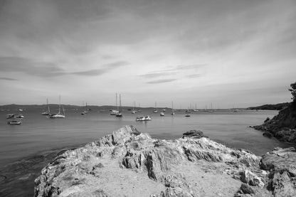 Avant-plan de roches sculptées et ligne de bateaux au large, ciel voilé à la presqu’île de Giens, noir et blanc
