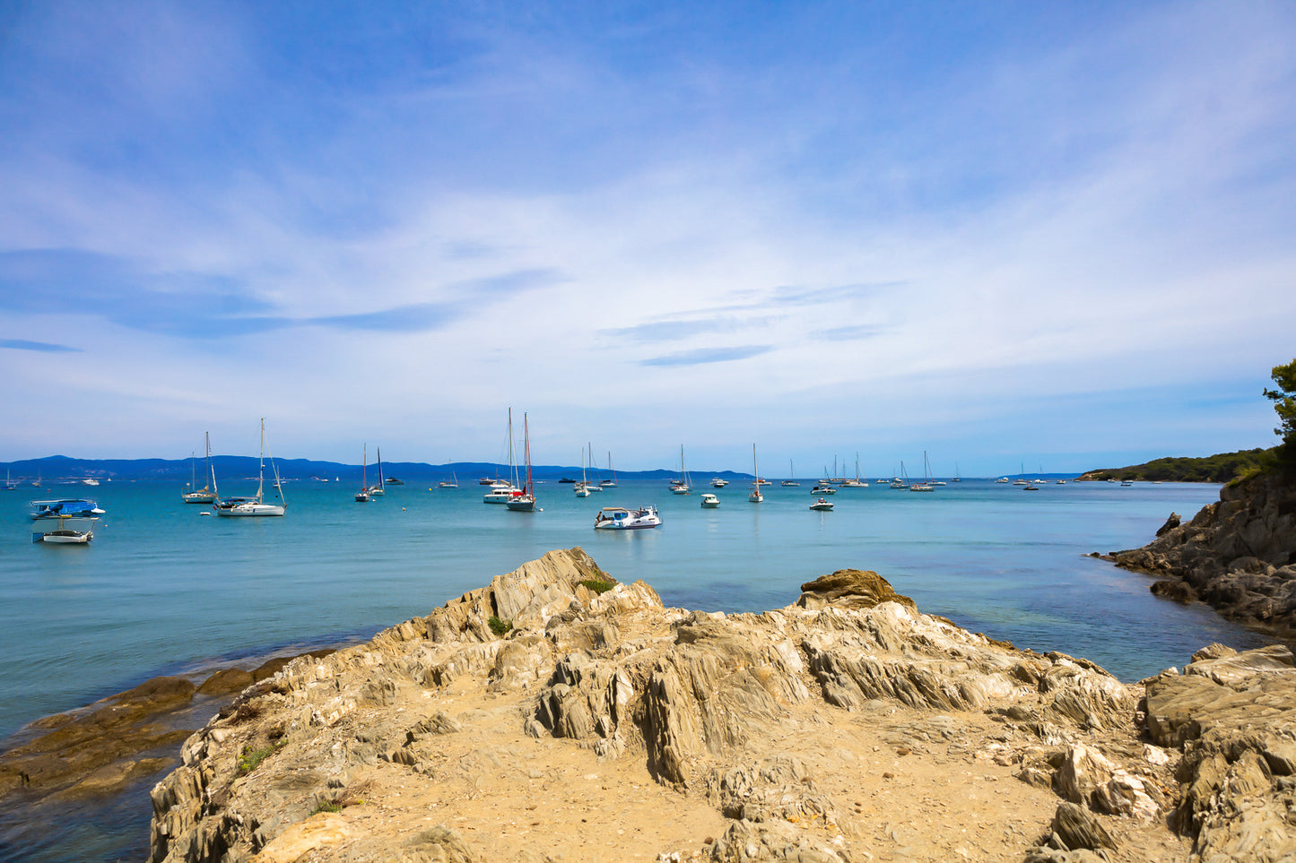 Avant-plan de roches sculptées et ligne de bateaux au large, ciel voilé à la presqu’île de Giens, couleur