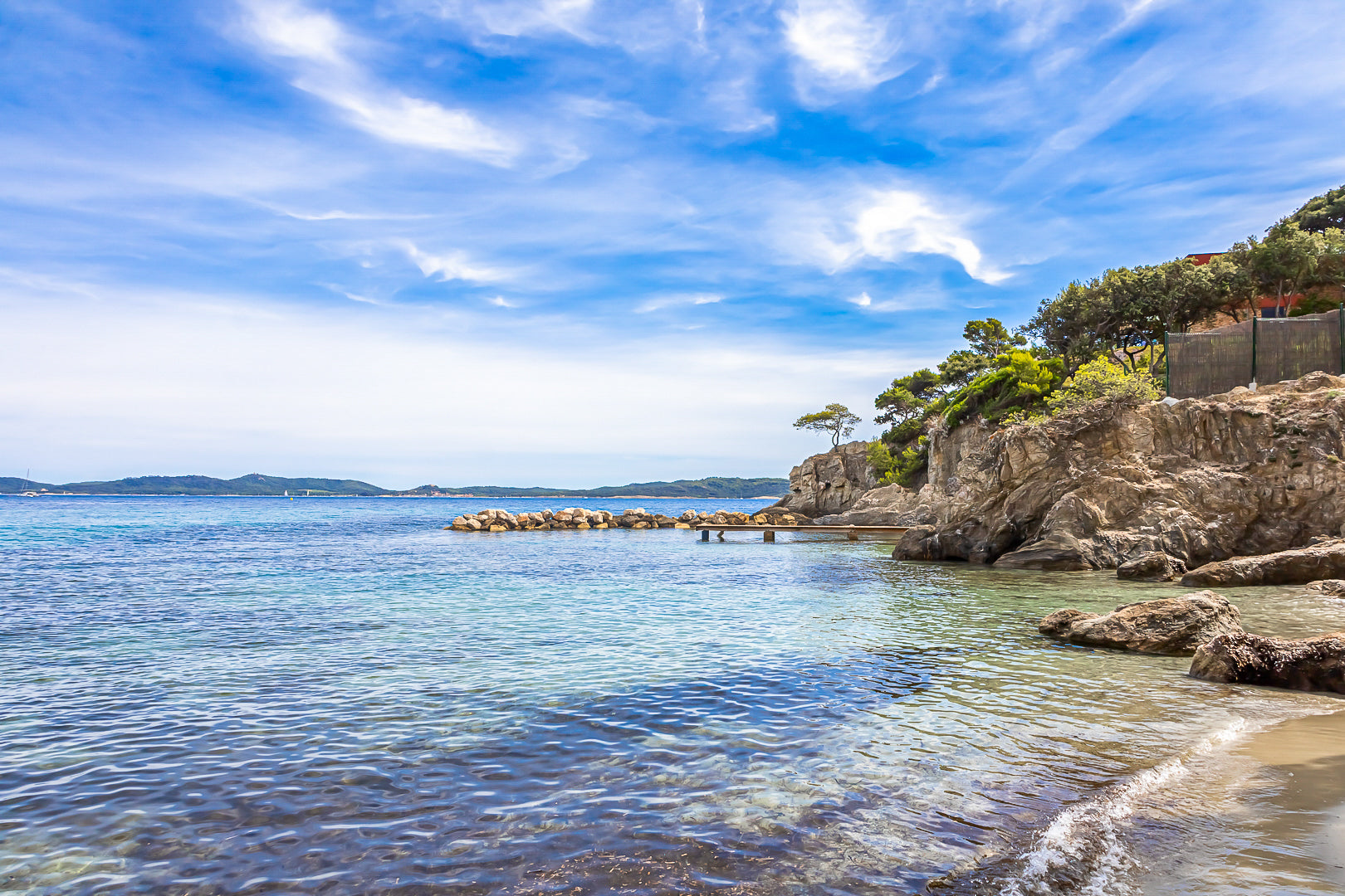 Petite crique bordée de rochers et pins, mer calme et nuages texturés à Giens, couleur