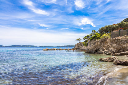 Petite crique bordée de rochers et pins, mer calme et nuages texturés à Giens, couleur