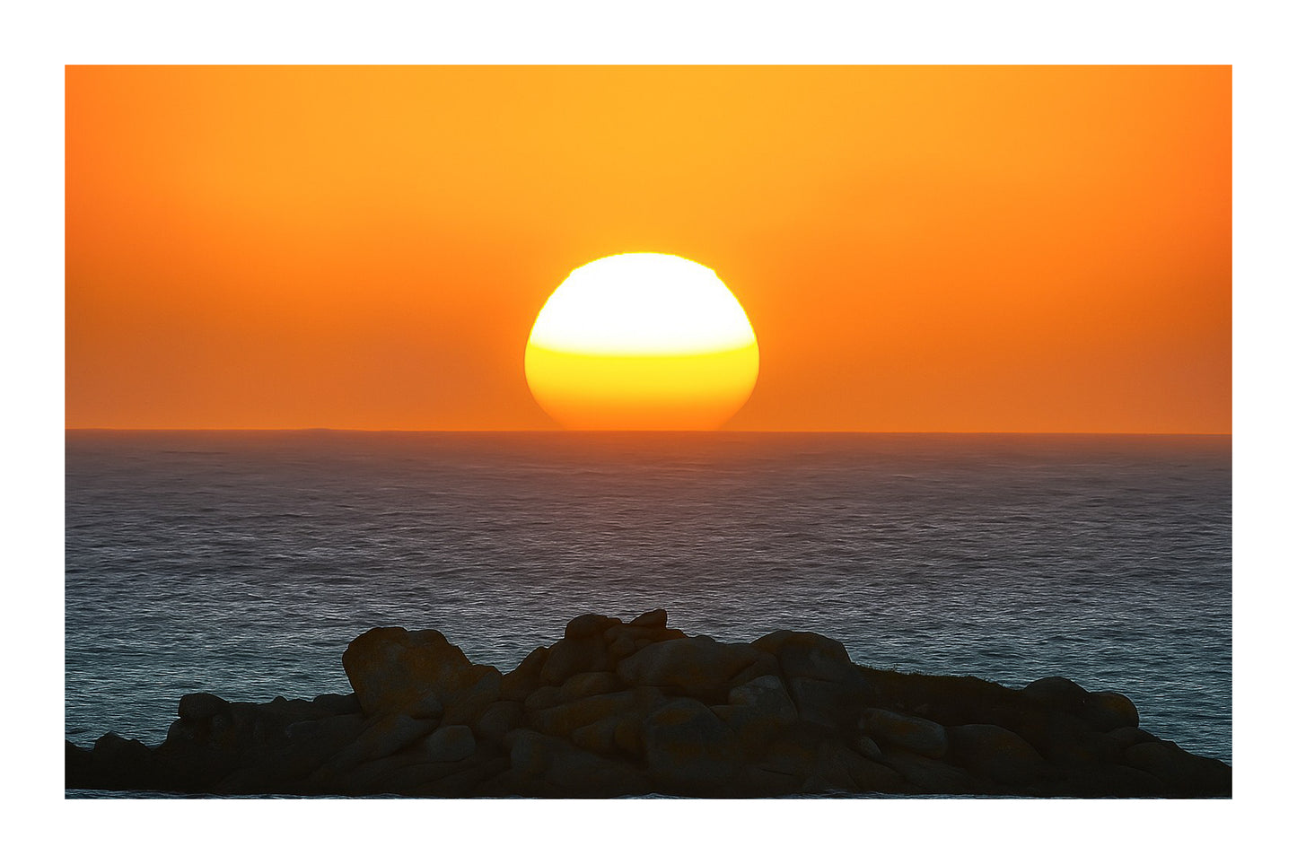 Soleil descendant sur la ligne d’horizon, illuminant la mer et un amas de rochers granitiques en Bretagne avec bordure