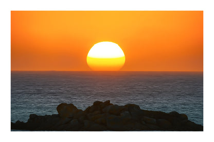 Soleil descendant sur la ligne d’horizon, illuminant la mer et un amas de rochers granitiques en Bretagne avec bordure