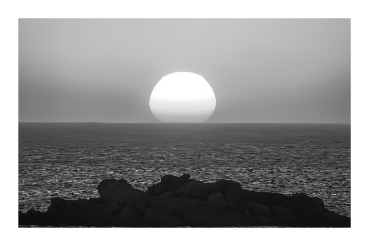 Soleil descendant sur la ligne d’horizon, illuminant la mer et un amas de rochers granitiques en Bretagne, noir et blanc avec bordure