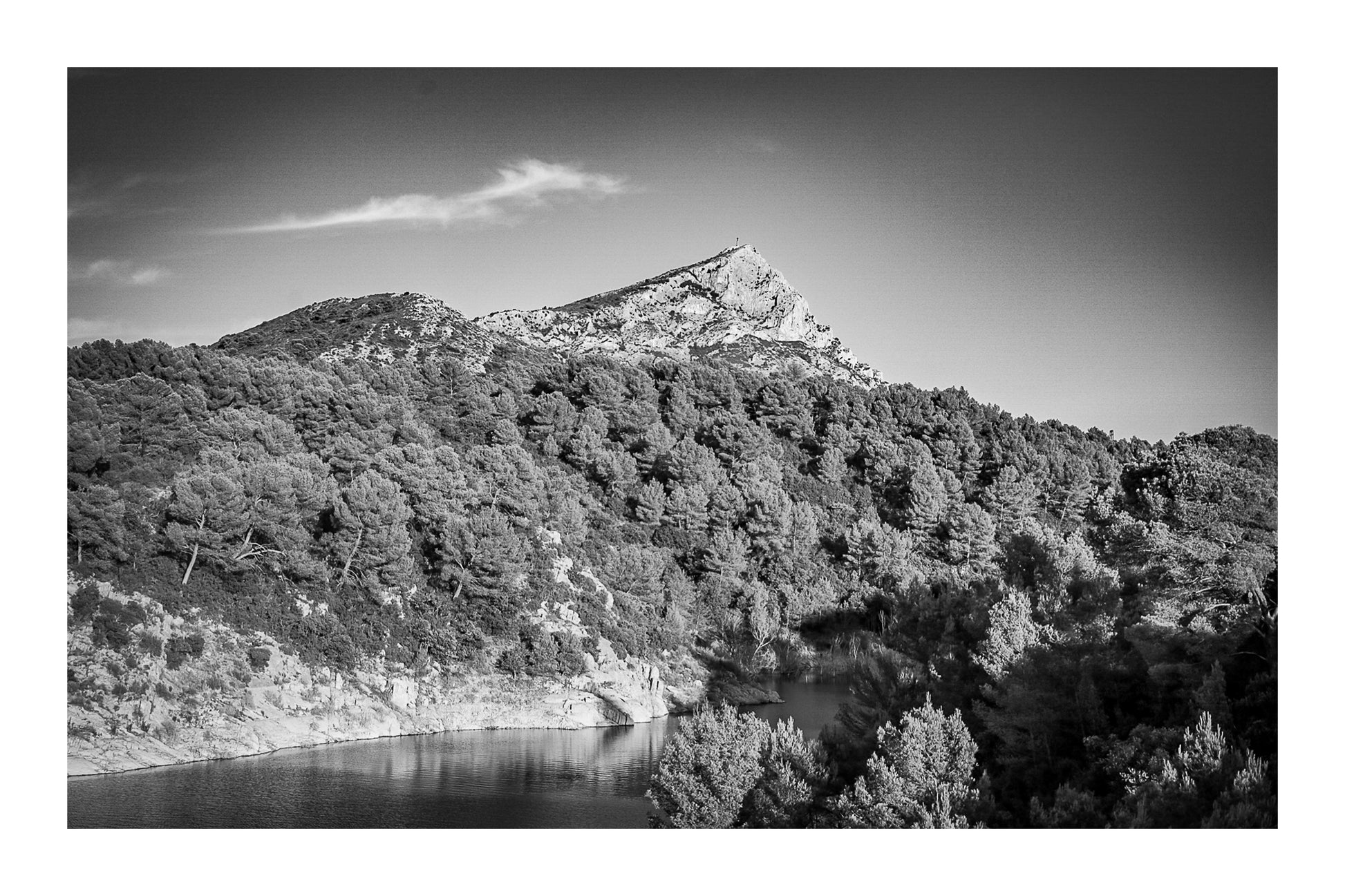 Vue de la montagne Sainte-Victoire dominant une colline de pins et un petit lac en contrebas sous un ciel bleu pur, noir et blanc avec bordure