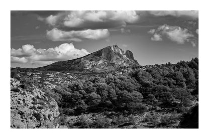 Montagne Sainte-Victoire se dressant au-dessus d’une forêt de pins, surmontée de gros nuages blancs, noir et blanc avec bordure