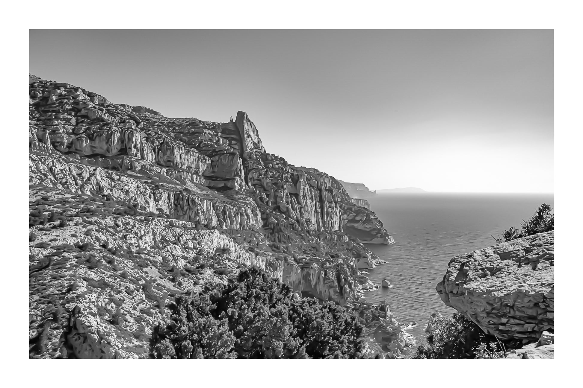 Falaises monumentales des calanques de Sugiton plongeant vers la Méditerranée par ciel bleu profond, noir et blanc avec bordure