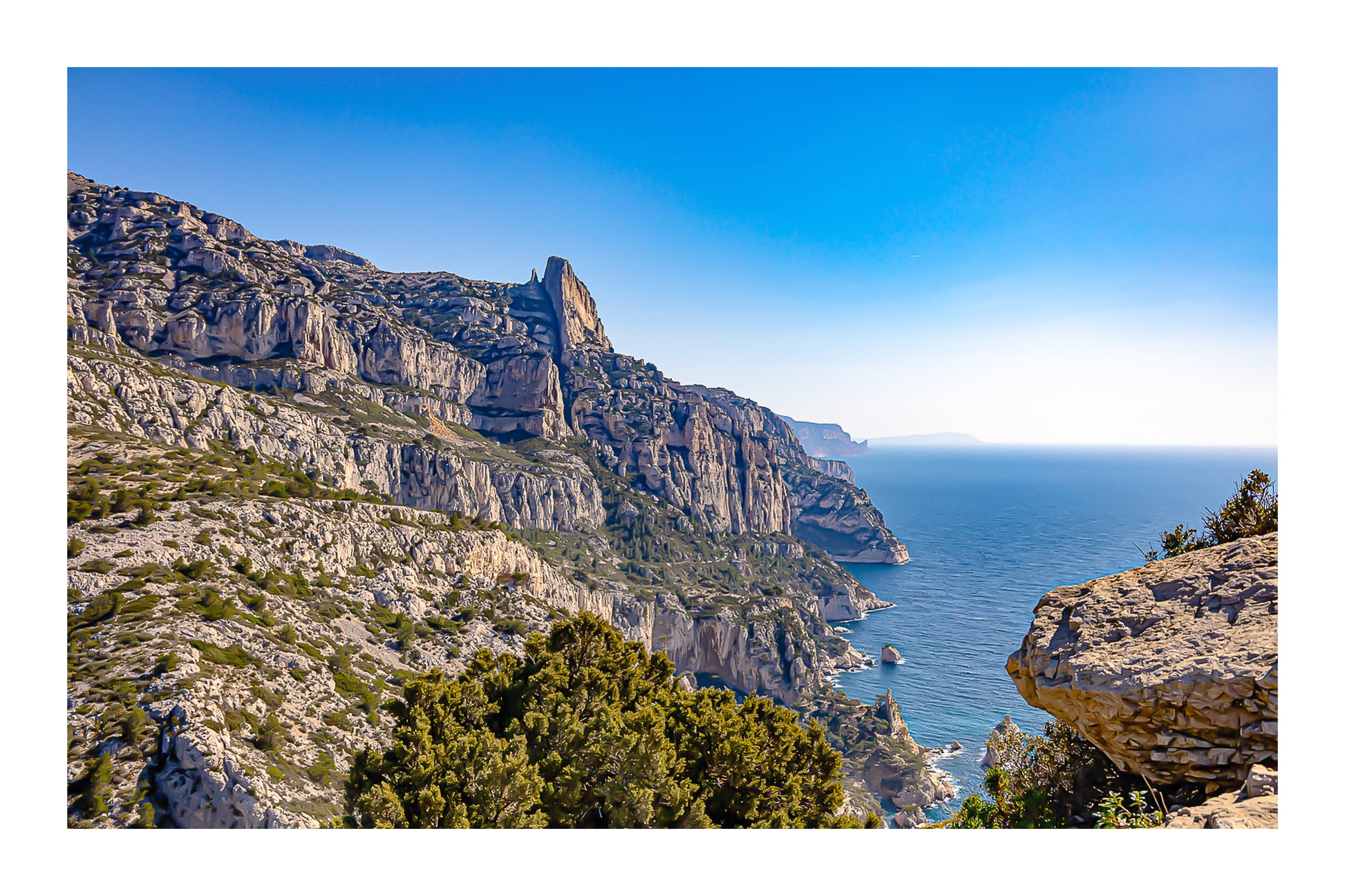 Falaises monumentales des calanques de Sugiton plongeant vers la Méditerranée par ciel bleu profond avec bordure