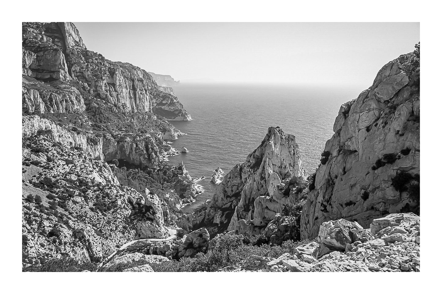Vue plongeante entre deux parois rocheuses sur l’eau turquoise de la calanque de Sugiton, noir et blanc avec bordure