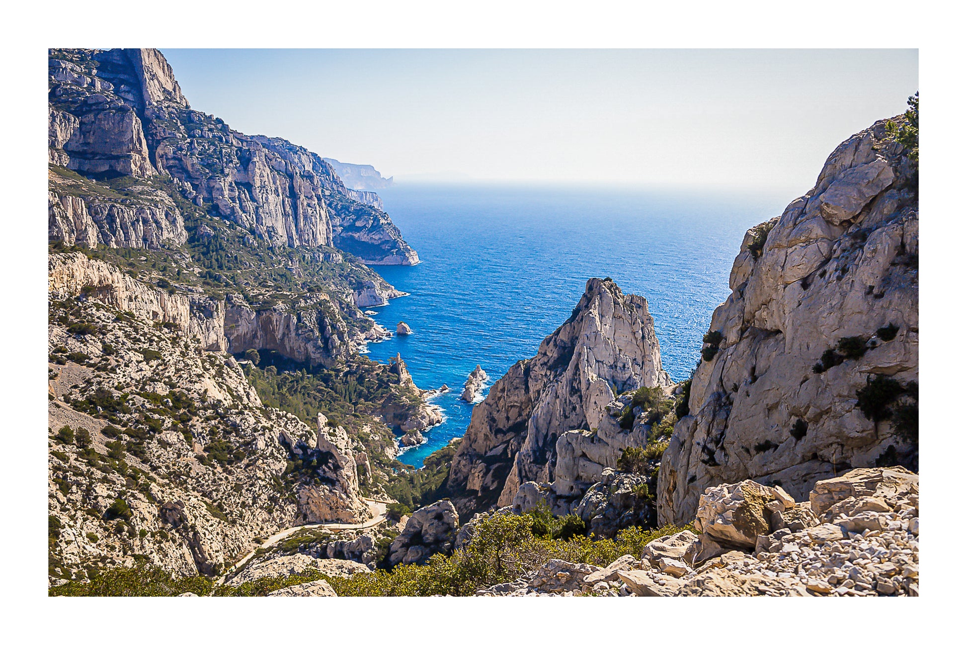 Vue plongeante entre deux parois rocheuses sur l’eau turquoise de la calanque de Sugiton avec bordure