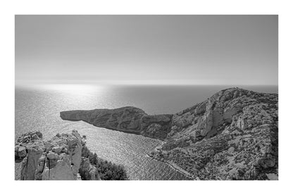 Éperon rocheux avançant dans la mer scintillante au large des calanques de Marseille, noir et blanc avec bordure