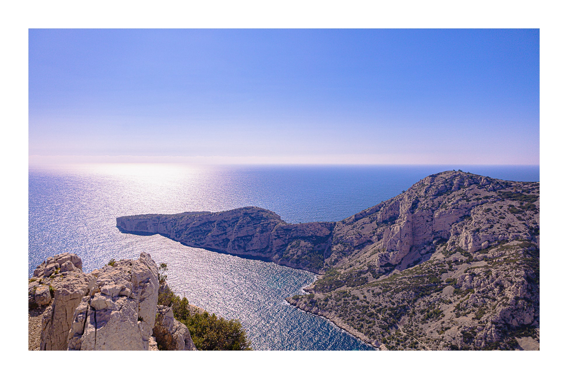 Éperon rocheux avançant dans la mer scintillante au large des calanques de Marseille avec bordure