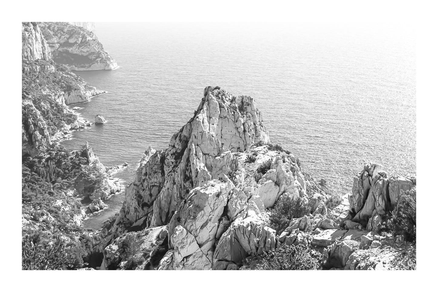 Pic calcaire élancé face à la mer, relief emblématique des calanques de Sugiton, noir et blanc avec bordure