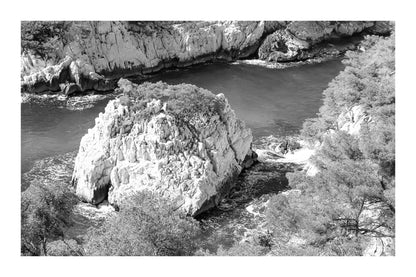 Petit îlot rocheux couvert de pins au centre d’une anse turquoise dans les calanques, noir et blanc avec bordure