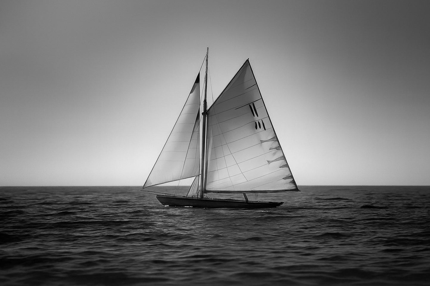 Voilier classique en navigation au coucher du soleil sur une mer calme en Méditerranée, voiles dorées par la lumière, noir et blanc