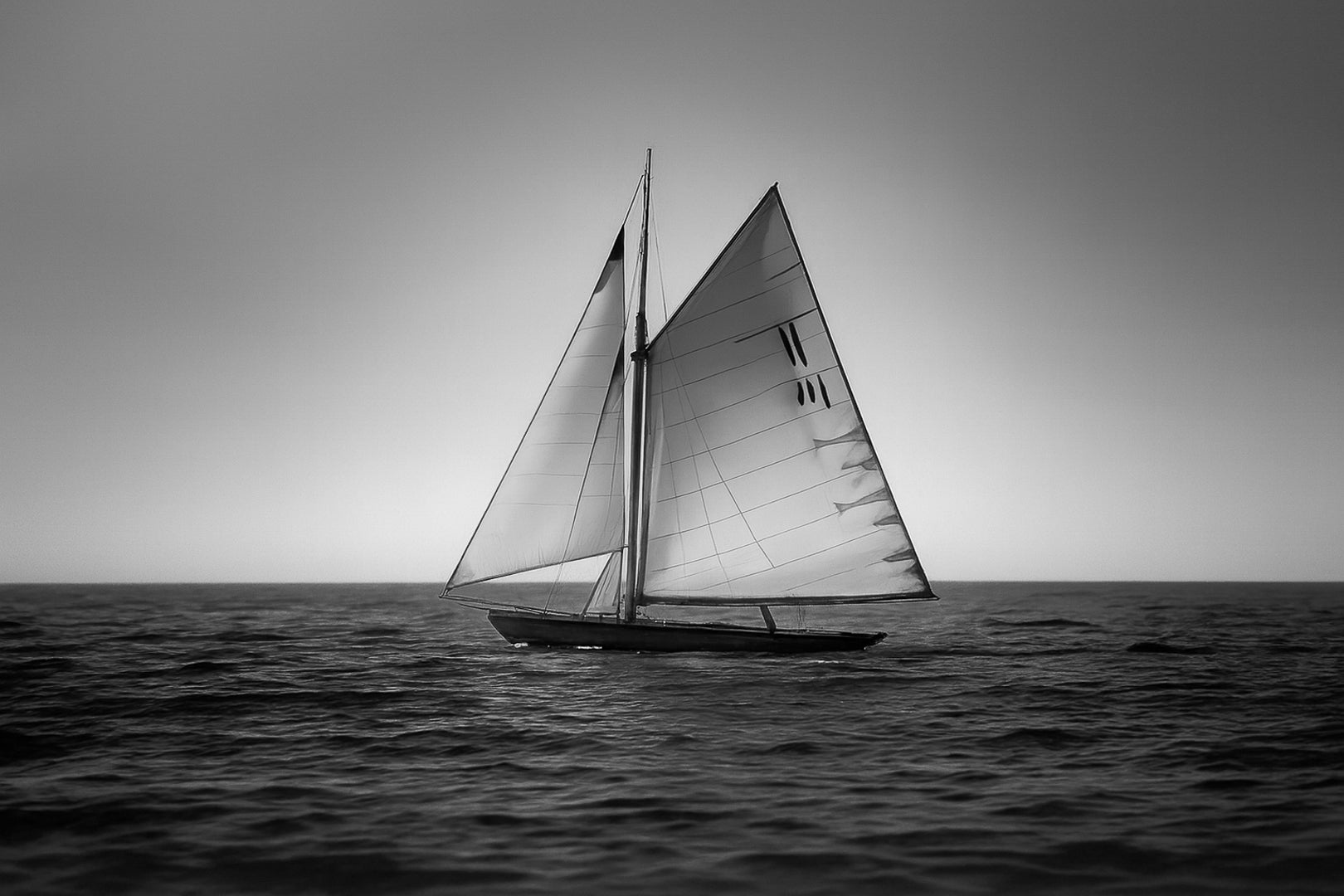 Voilier classique en navigation au coucher du soleil sur une mer calme en Méditerranée, voiles dorées par la lumière, noir et blanc