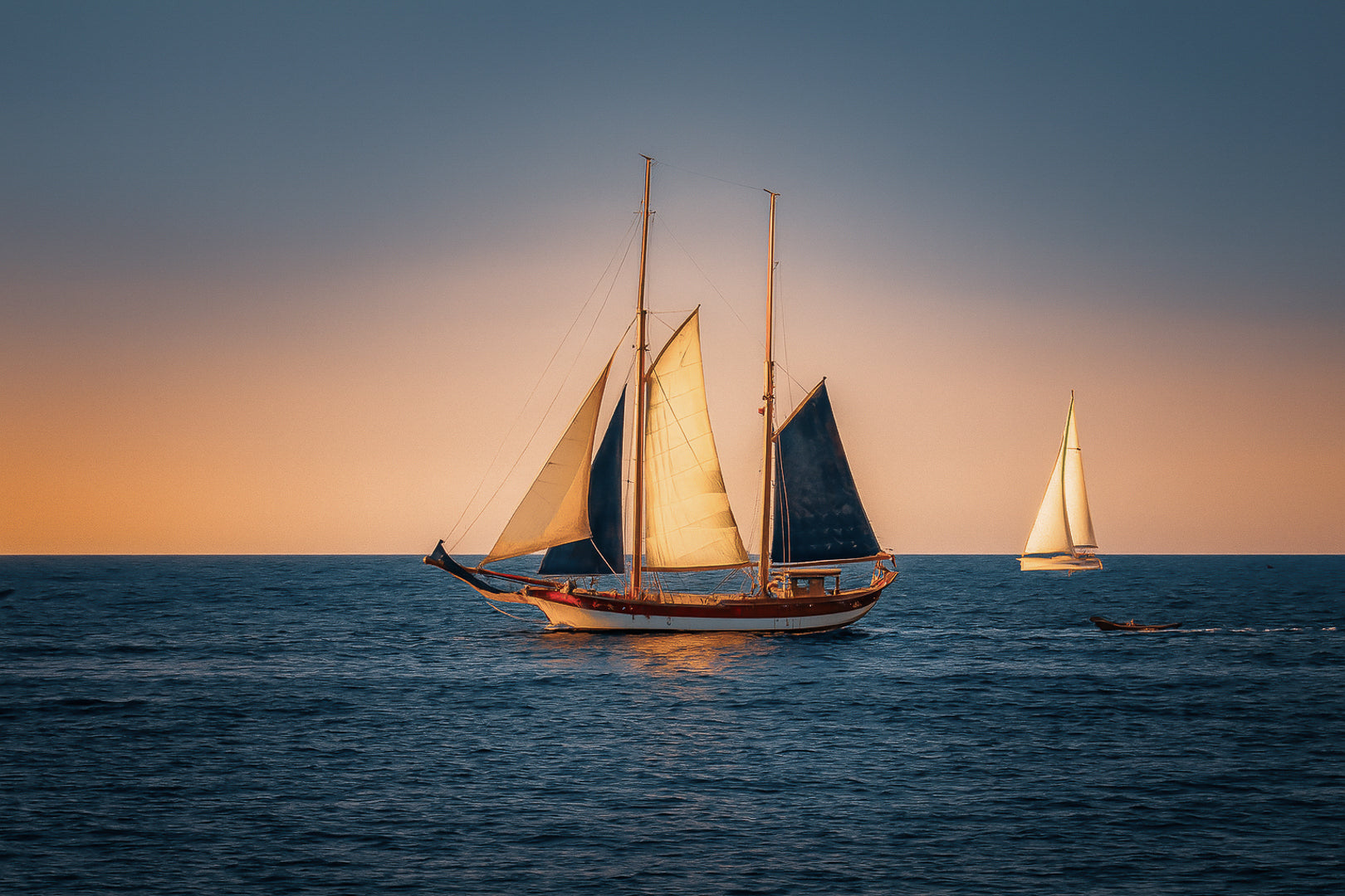Deux voiliers traditionnels naviguant au large au crépuscule, ciel dégradé et reflets chauds sur la Méditerranée