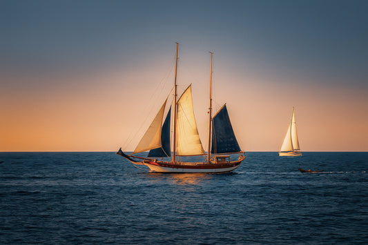 Deux voiliers traditionnels naviguant au large au crépuscule, ciel dégradé et reflets chauds sur la Méditerranée
