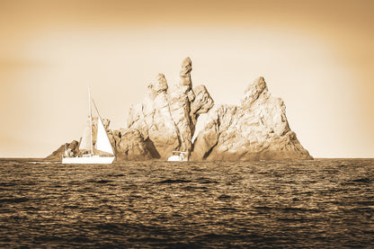 Voilier longeant un massif rocheux percé d’une arche en Méditerranée, lumière rasante de fin de journée, vintage