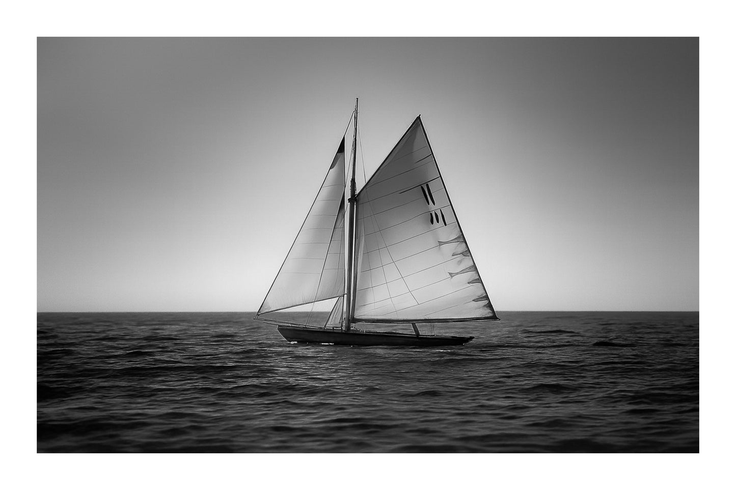 Voilier classique en navigation au coucher du soleil sur une mer calme en Méditerranée, voiles dorées par la lumière, noir et blanc avec bordure