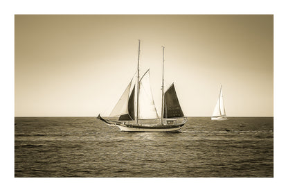 Deux voiliers traditionnels naviguant au large au crépuscule, ciel dégradé et reflets chauds sur la Méditerranée, vintage avec bordure