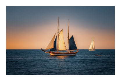 Deux voiliers traditionnels naviguant au large au crépuscule, ciel dégradé et reflets chauds sur la Méditerranée avec bordure