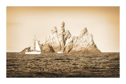 Voilier longeant un massif rocheux percé d’une arche en Méditerranée, lumière rasante de fin de journée, vintage avec bordure